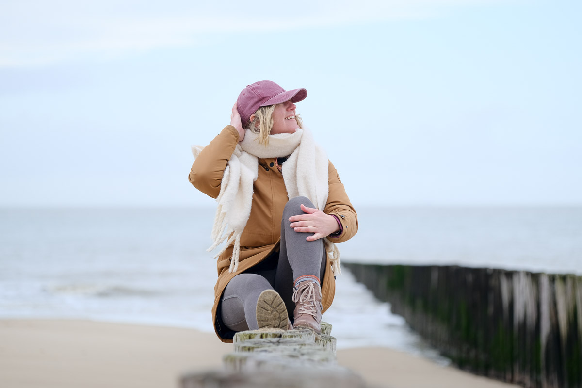 Alleine ans Meer im Winter – Frau sitzt entspannt am Strand und blickt auf die Nordsee